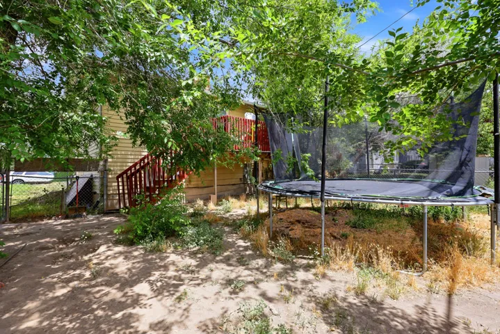Expansive backyard featuring mature trees, a multi-level wooden deck with red railings, and a fenced perimeter