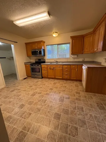 Kitchen featuring wood cabinetry, stainless steel range and microwave, dual basin sink, and tile-pattern flooring