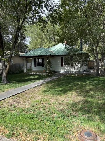 Front exterior with white siding, a green metal roof, and dark window shutters