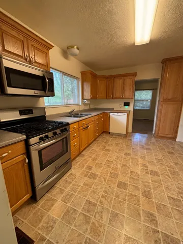 Kitchen featuring ample wood cabinetry, stainless steel range with microwave, integrated dishwasher, and patterned tile flooring