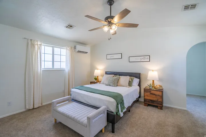 Carpeted interior featuring a ceiling fan with integrated lighting, a window with grid panes, an arched doorway, and an installed wall-mounted air conditioning unit