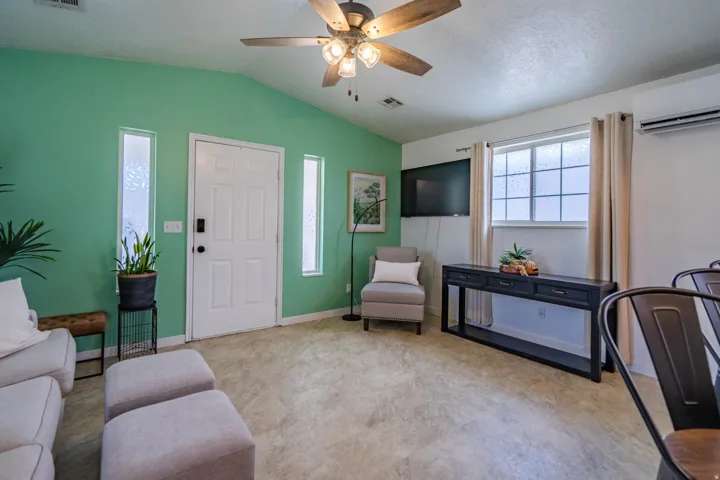 Bright and spacious recreation room featuring vibrant sage green accent wall, ceiling fan with integrated lighting, and neutral wood-finish flooring throughout