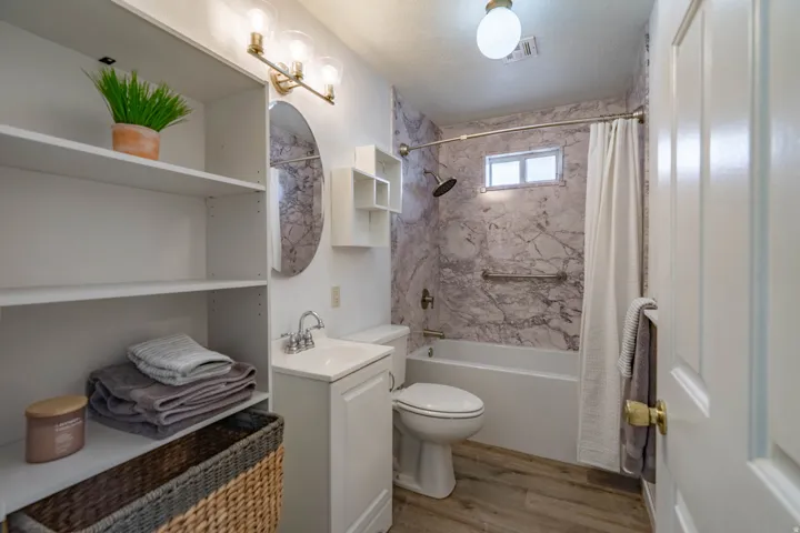 Full bathroom featuring a white vanity with integrated sink, wood-finish flooring, and a tub/shower combination with a marbled wall surround