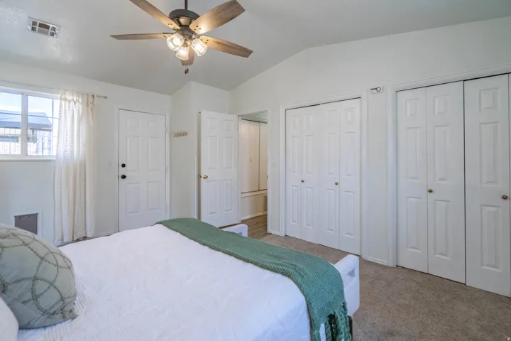 Spacious primary bedroom featuring neutral carpeting, a ceiling fan with integrated lighting, and multiple closet spaces with six-panel doors