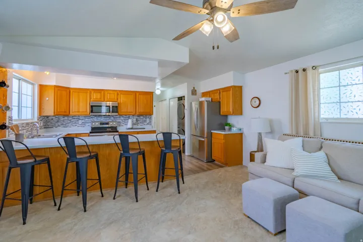 Open-concept living space featuring a chef's kitchen with warm wood cabinetry, stainless steel appliances, and a tile backsplash anchored by a generously sized island with seating for multiple guests
