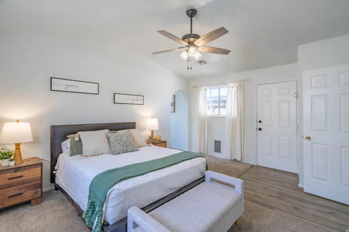 Spacious bedroom featuring a vaulted ceiling with a ceiling fan, a window with natural light, and a paneled entry door