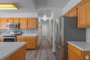 Kitchen featuring warm wood cabinetry, stainless steel appliances, a mosaic tile backsplash, and light countertops