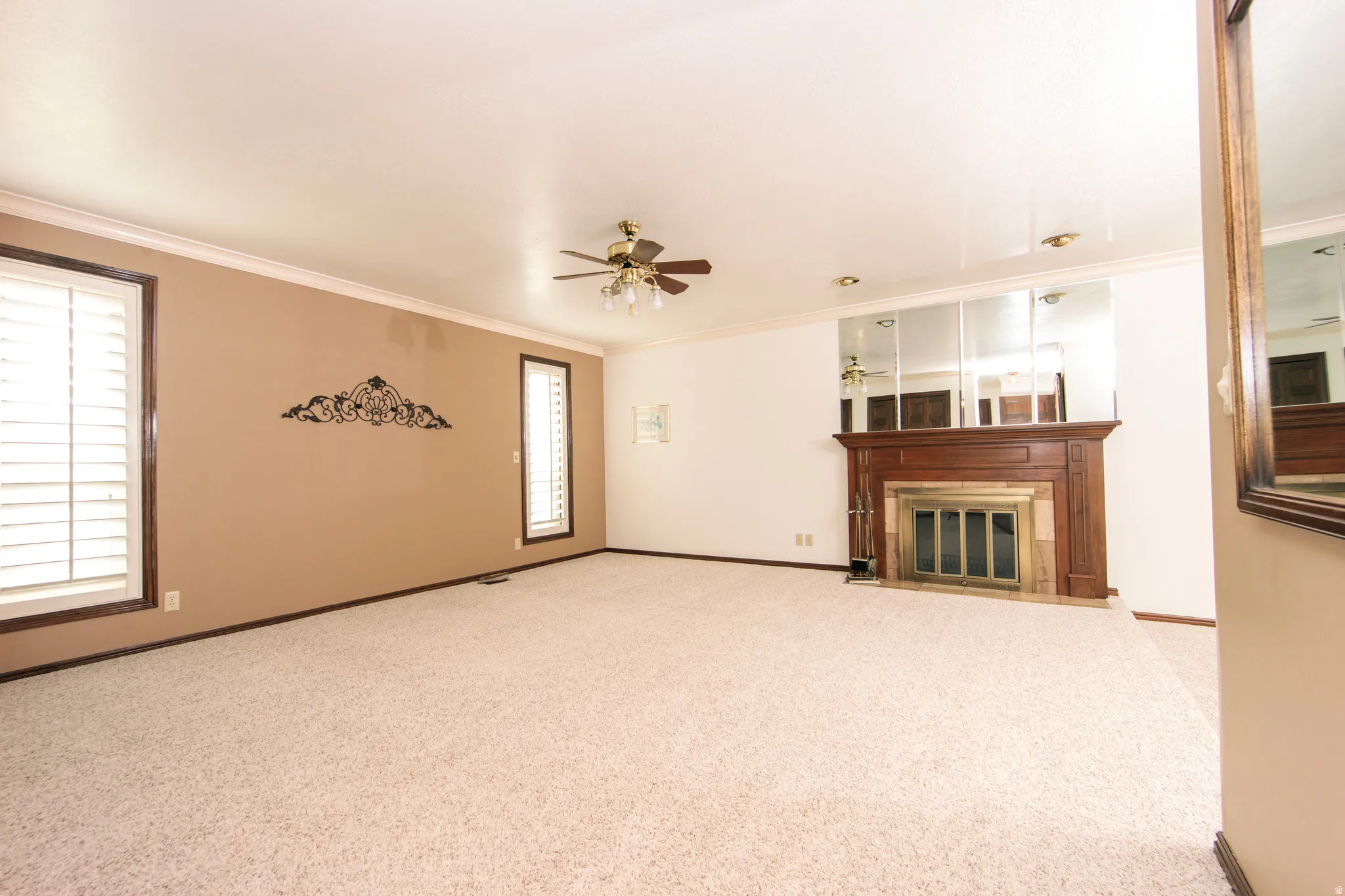 Spacious carpeted interior featuring a wood-mantled fireplace, mirrored accent wall, and ceiling fan with integrated lighting