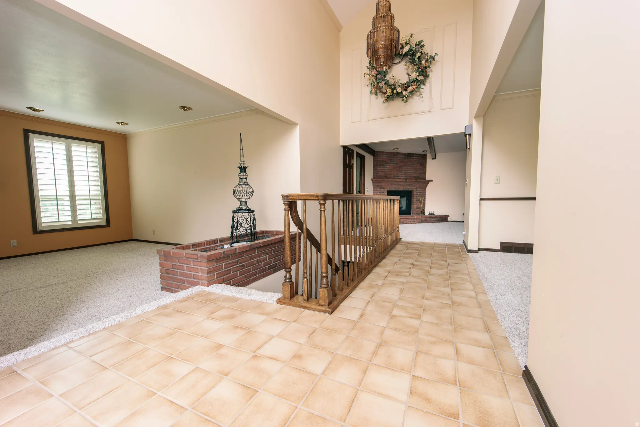 Foyer entrance featuring light-toned tile flooring, a wooden banister, and a brick-faced planter