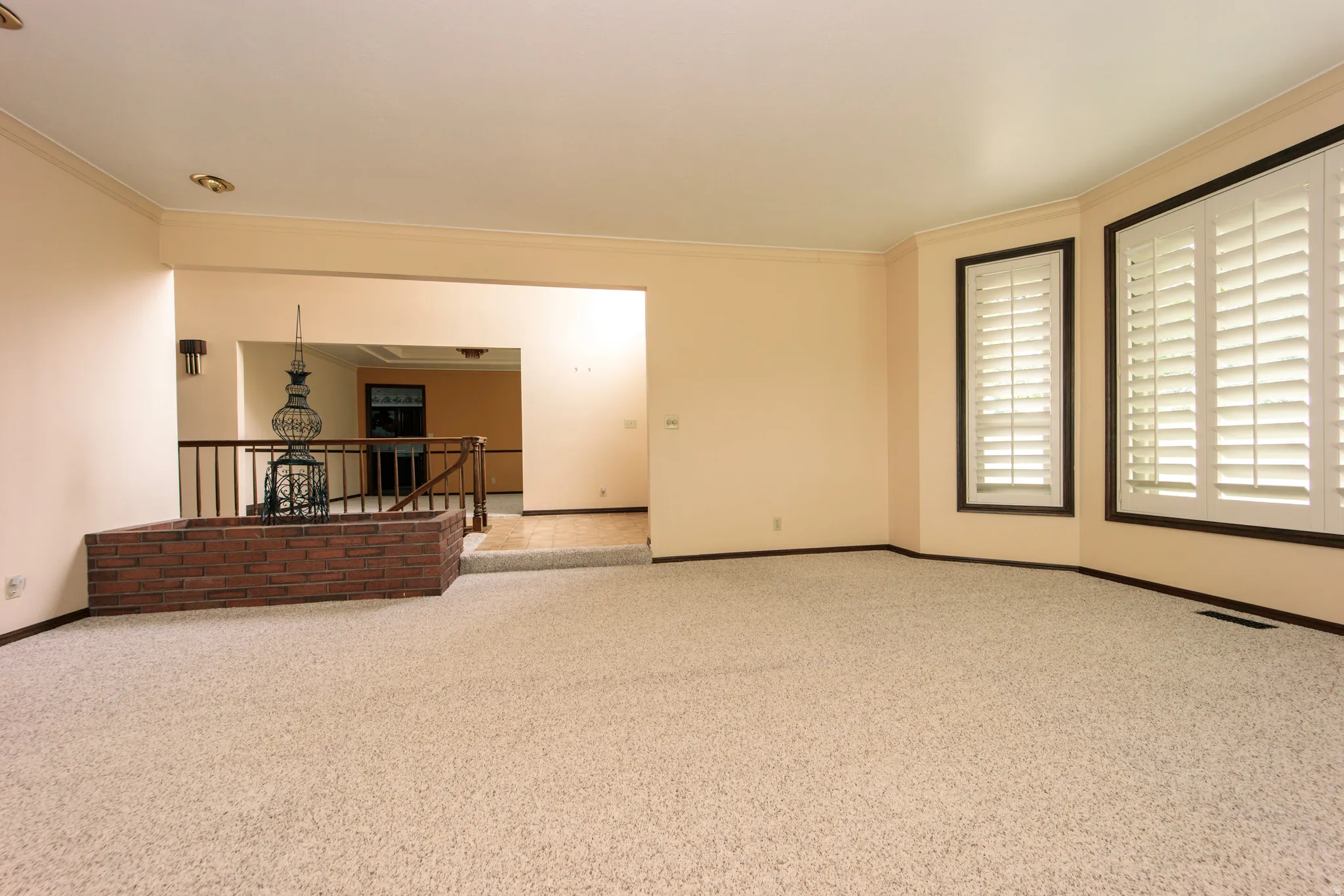 Spacious living area featuring neutral carpeting, a decorative brick planter, and a half-wall with iron railing