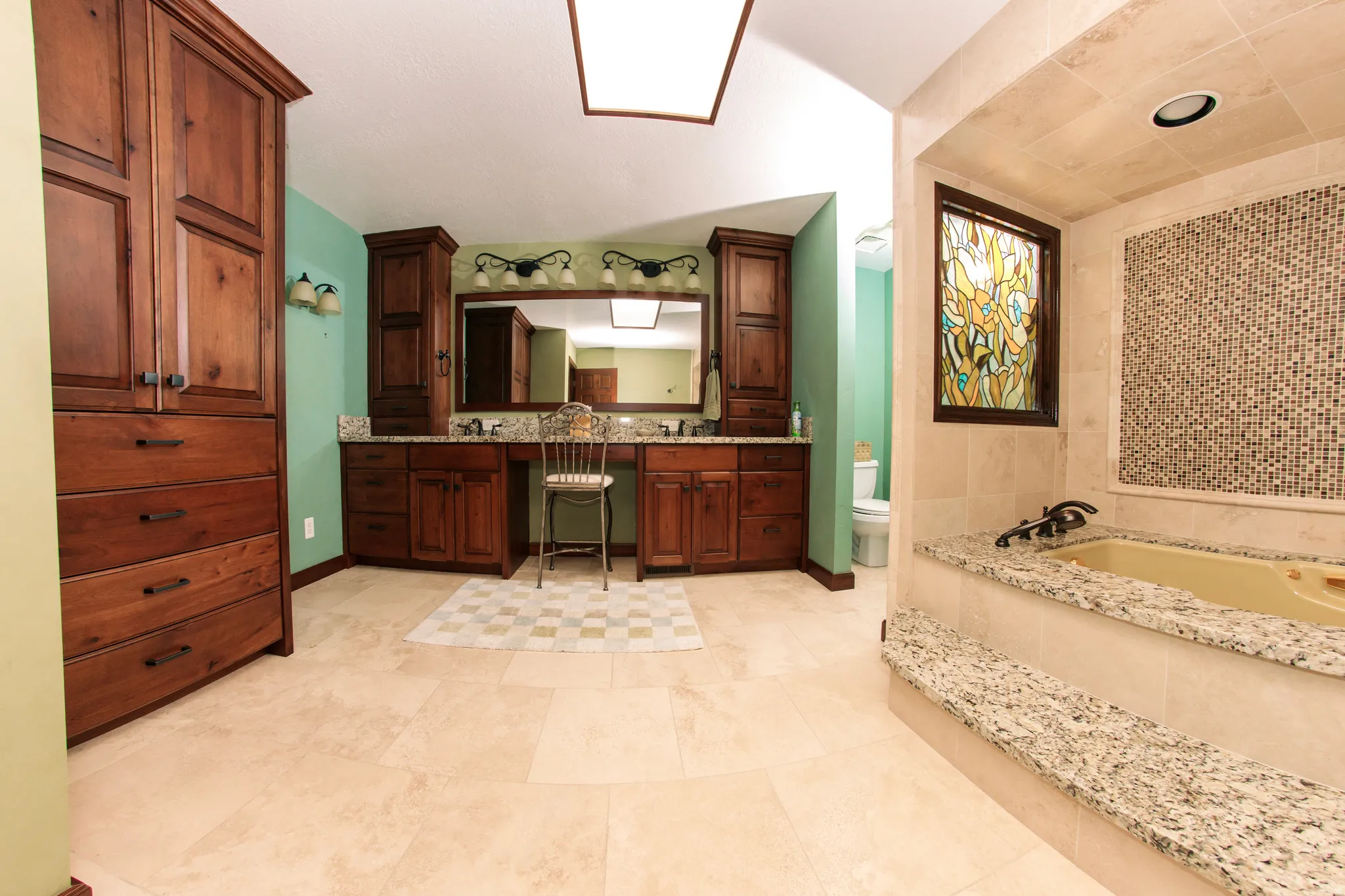 Spacious bathroom featuring light-toned tile flooring, extensive wood cabinetry, and a double vanity with granite-finish countertops