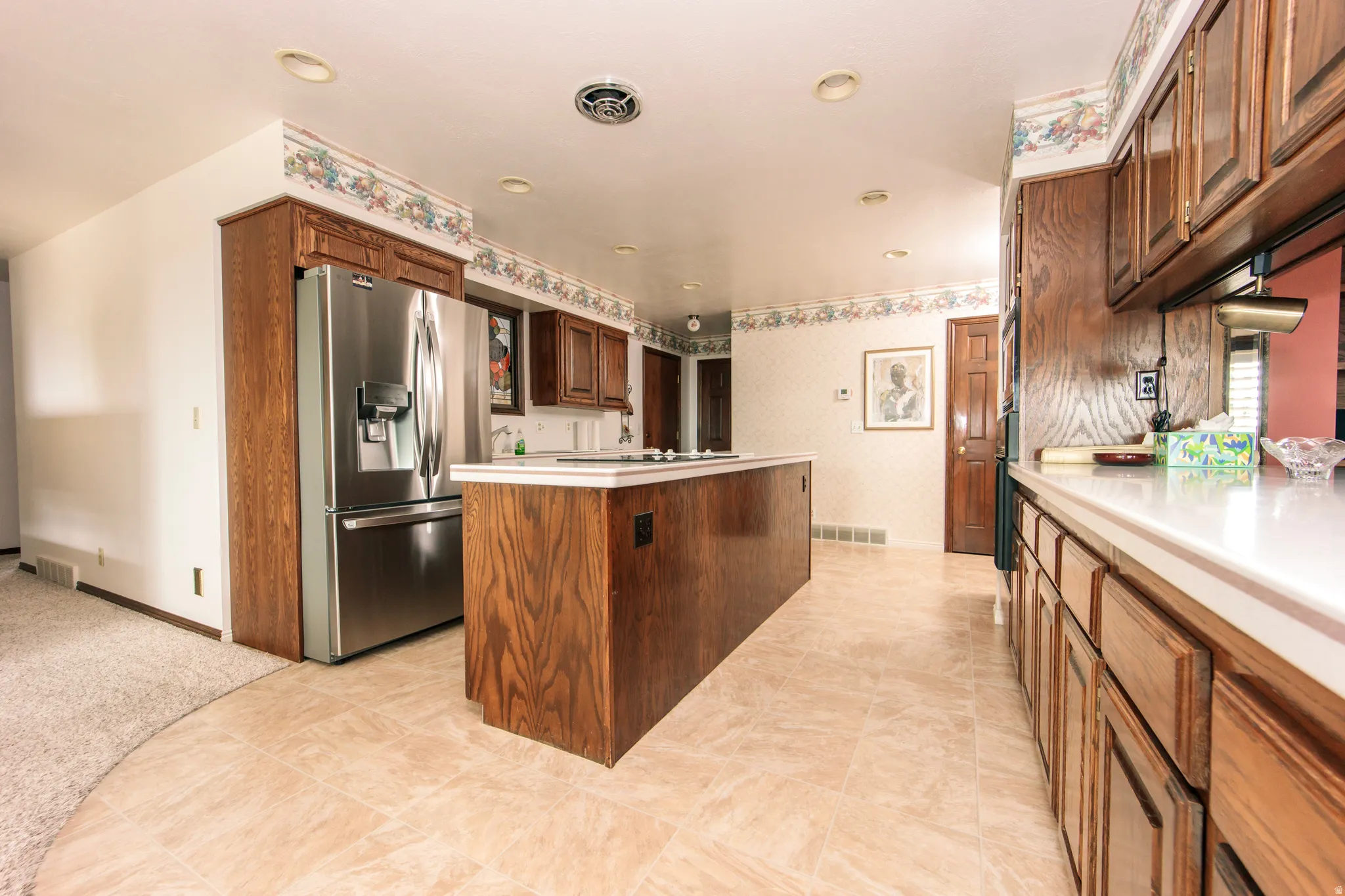 Kitchen featuring light-toned tile flooring, wood cabinetry, an integrated stainless steel refrigerator, white countertops, and recessed lighting
