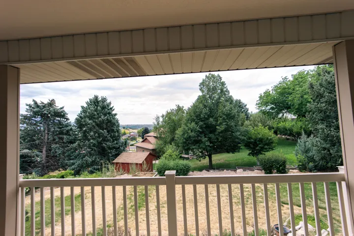 Outdoor balcony with white railing, overlooking varied mature trees, natural landscaping, and distant structures