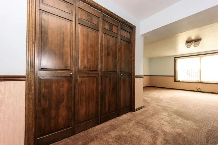 Wood-panel bi-fold closet doors with brass hardware, textured wall paneling, and wall-to-wall carpeting throughout