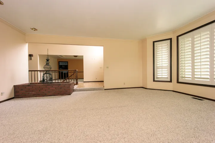 Spacious living area featuring neutral carpeting, a decorative brick planter, and a half-wall with iron railing