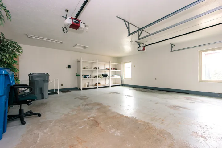 Spacious garage featuring white painted walls, two windows, two garage door openers, and built-in shelving
