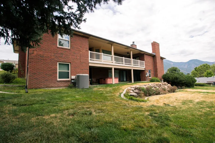 Brick exterior residence featuring a covered balcony with white railing, lower level patio access, and a rock-lined garden bed