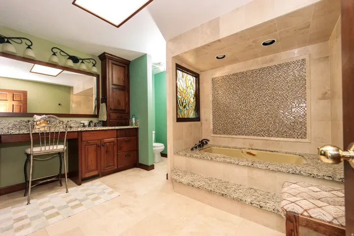 Bathroom featuring a built-in soaking tub with mosaic tile surround, wood-finish cabinetry, stone countertops, and recessed lighting