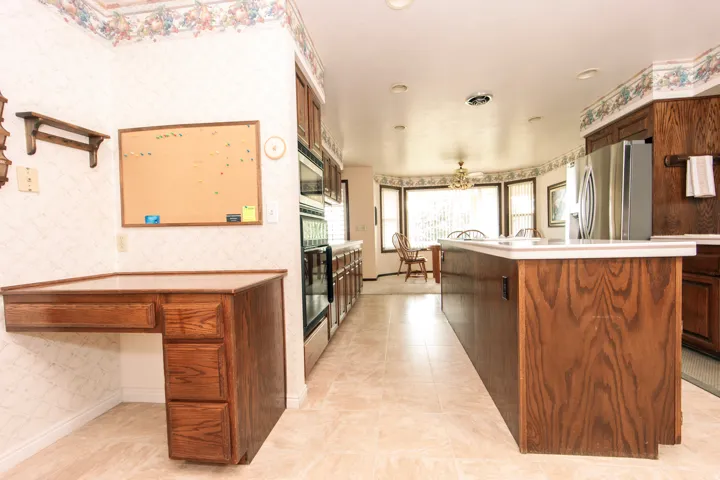 Spacious kitchen featuring an extended island with white countertops, integrated stainless steel appliances, wood-finish cabinetry, and recessed lighting