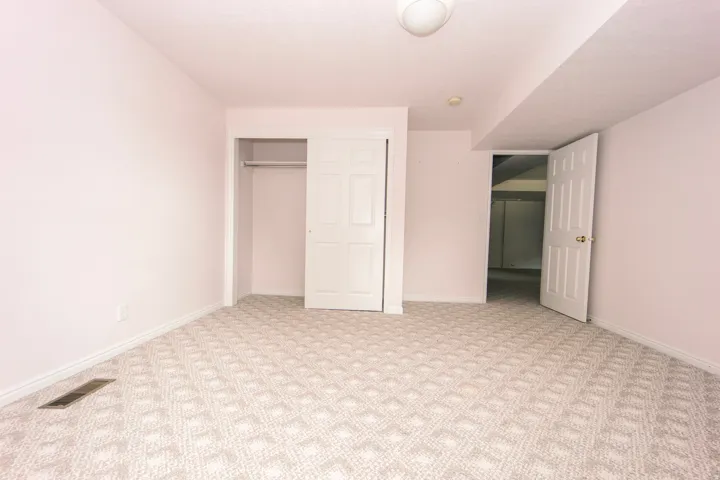 Carpeted interior space featuring a geometric pattern, white baseboards, and a built-in closet with bi-fold doors