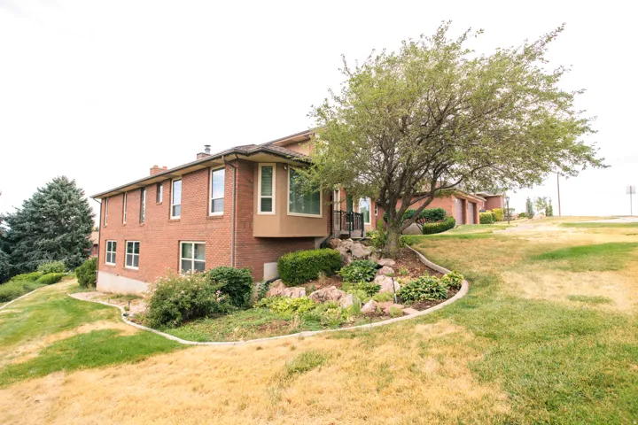 Brick exterior residence featuring multiple windows, a bay window, a mature tree, and sloped landscaping