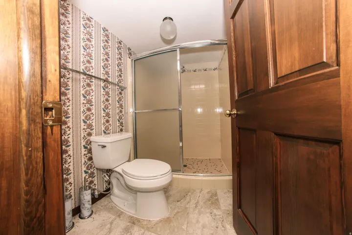 Bathroom featuring a white toilet, patterned wallpaper, and a shower with frosted glass enclosure