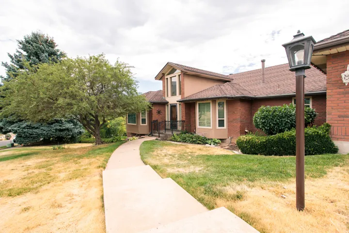 Traditional brick residence featuring a brown shingle roof, bay windows, and a concrete pathway leading to the entrance