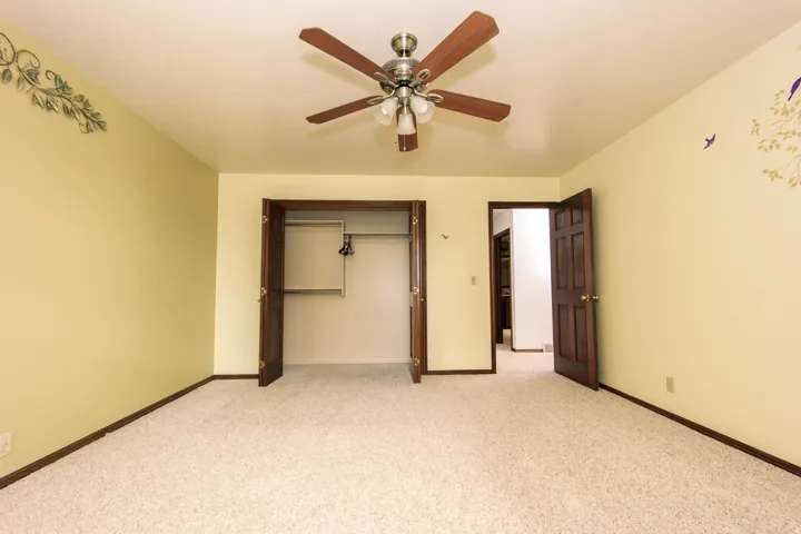 Carpeted room featuring a ceiling fan with integrated lighting, a spacious closet with bi-fold doors, and a solid wood paneled door