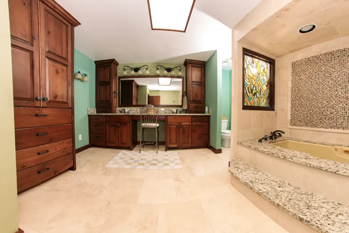Spacious bathroom featuring light-toned tile flooring, extensive wood cabinetry, and a double vanity with granite-finish countertops
