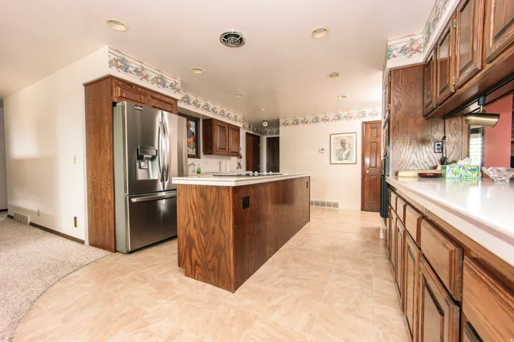 Kitchen featuring light-toned tile flooring, wood cabinetry, an integrated stainless steel refrigerator, white countertops, and recessed lighting
