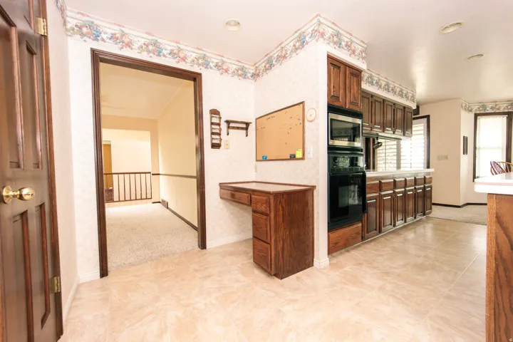 Kitchen area featuring wood cabinetry, built-in oven and microwave, and light-toned tile flooring