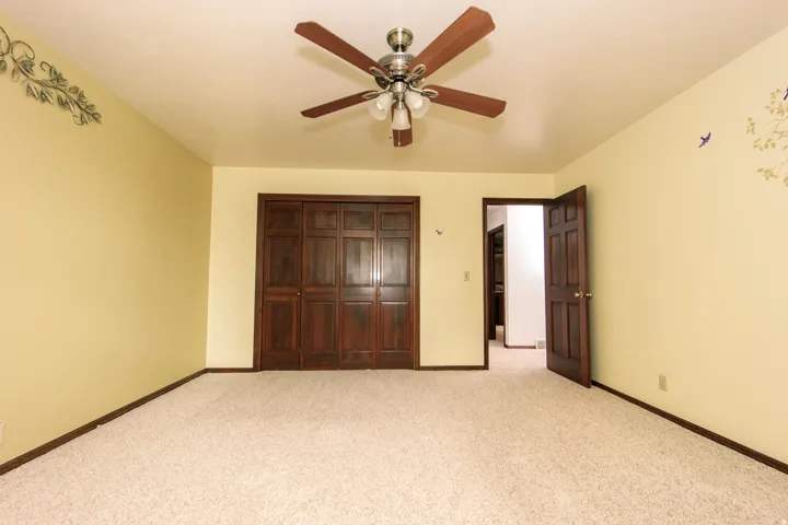 Carpeted room featuring a ceiling fan with integrated lighting, dark wood bi-fold closet doors, and dark wood trim