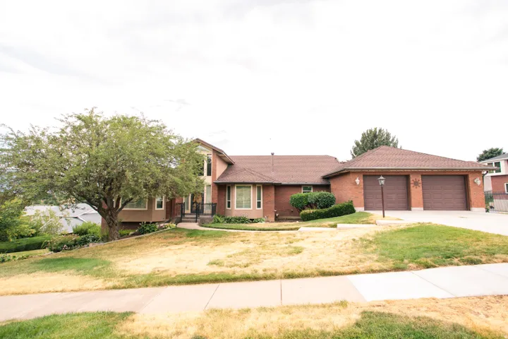 Brick exterior home featuring a two-car garage, mature front yard tree, and an inviting front entrance