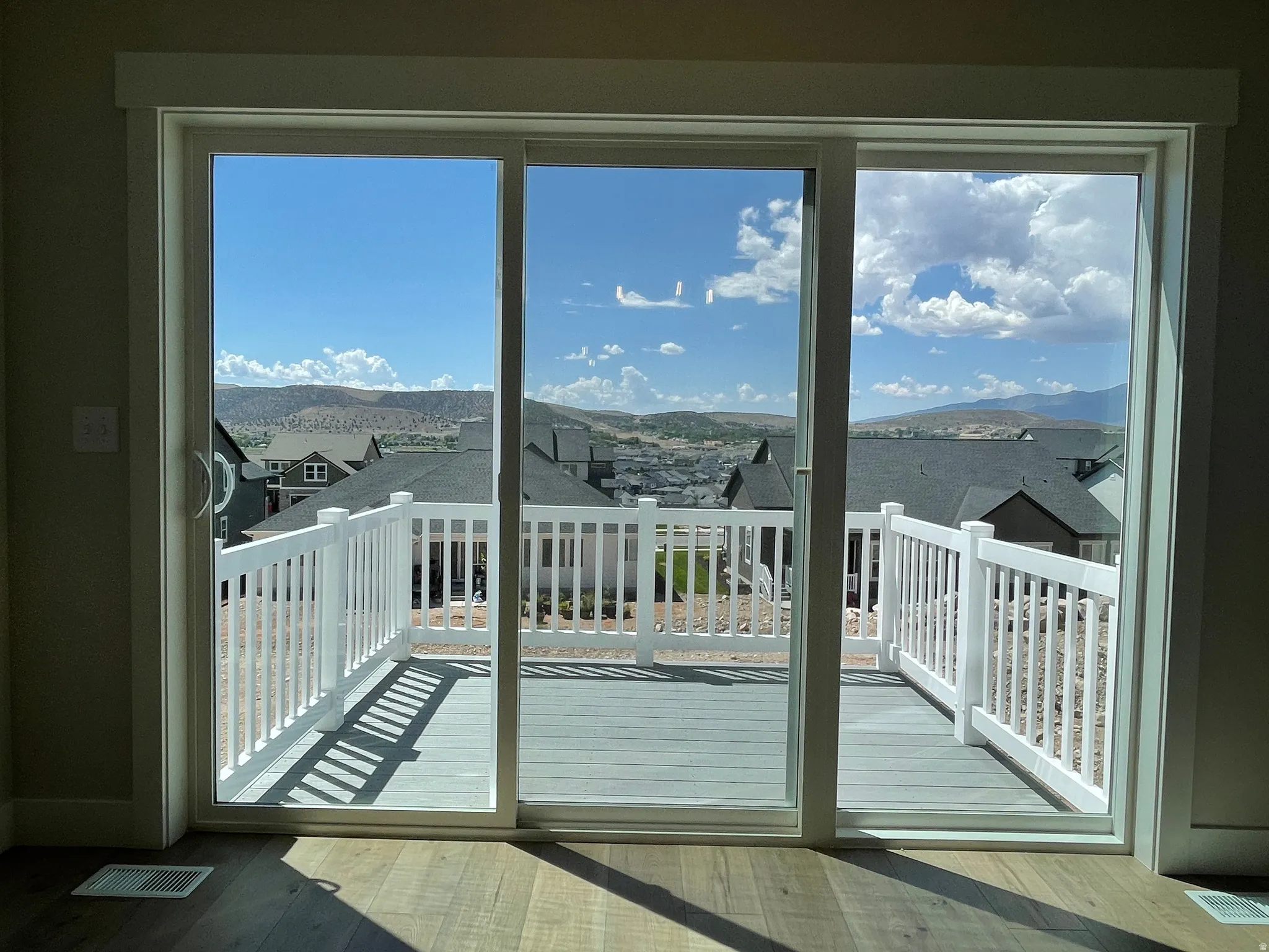 Sliding glass door opening to an outdoor deck with white railing, featuring wood-finish flooring and expansive mountain scenery