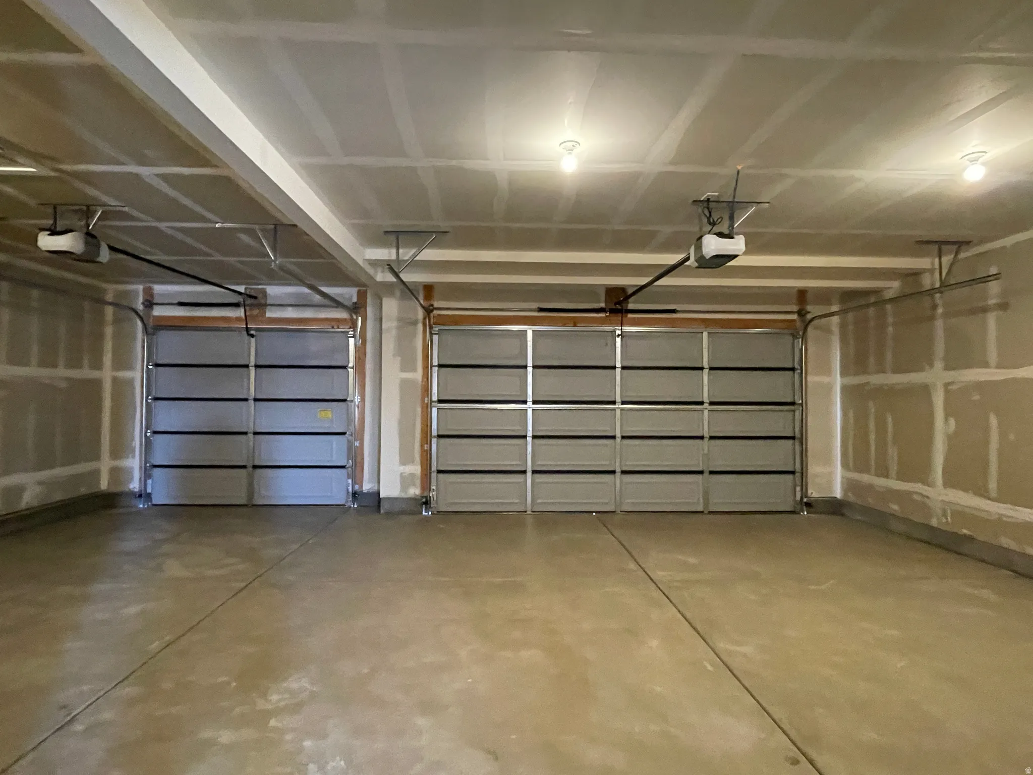 Spacious garage featuring two overhead doors, automatic openers, exposed ceiling joists, and concrete flooring