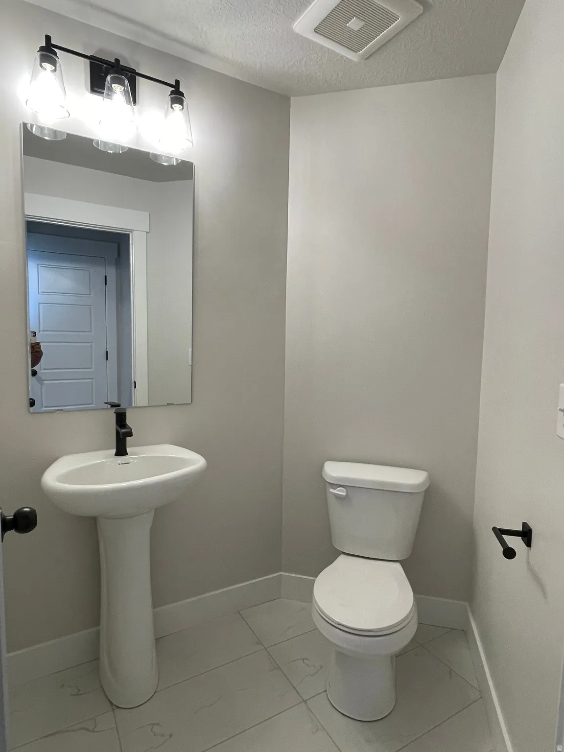 Pedestal sink with a matte black faucet, wall-mounted mirror, and three-light vanity fixture