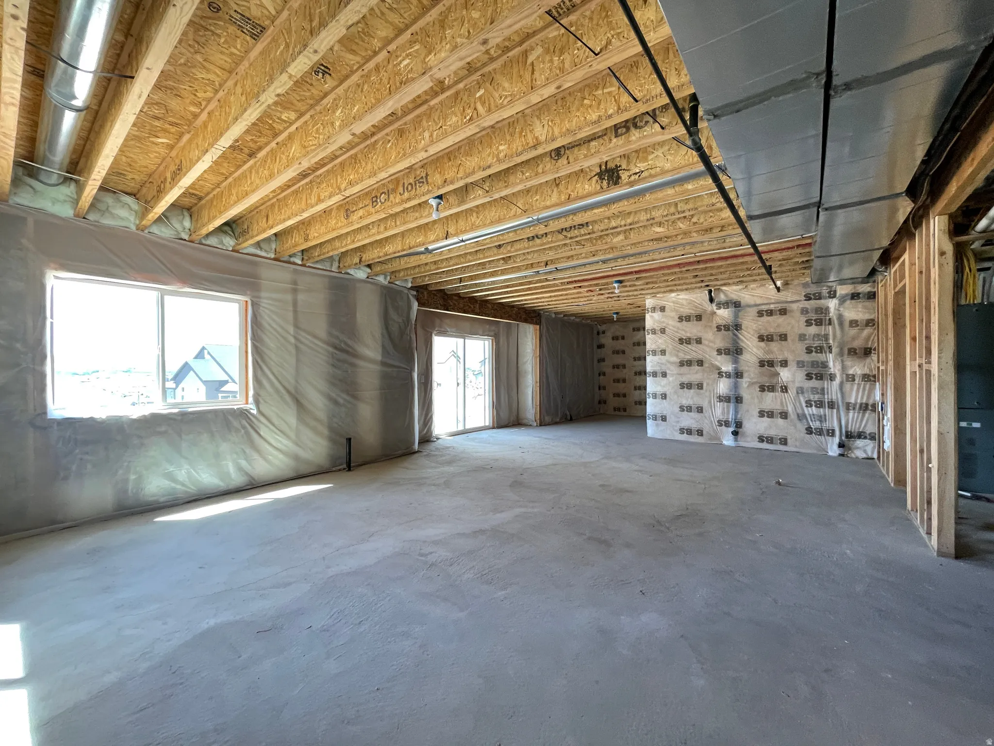 Unfinished lower level featuring exposed wood joists, concrete flooring, dual windows, and a sliding glass door