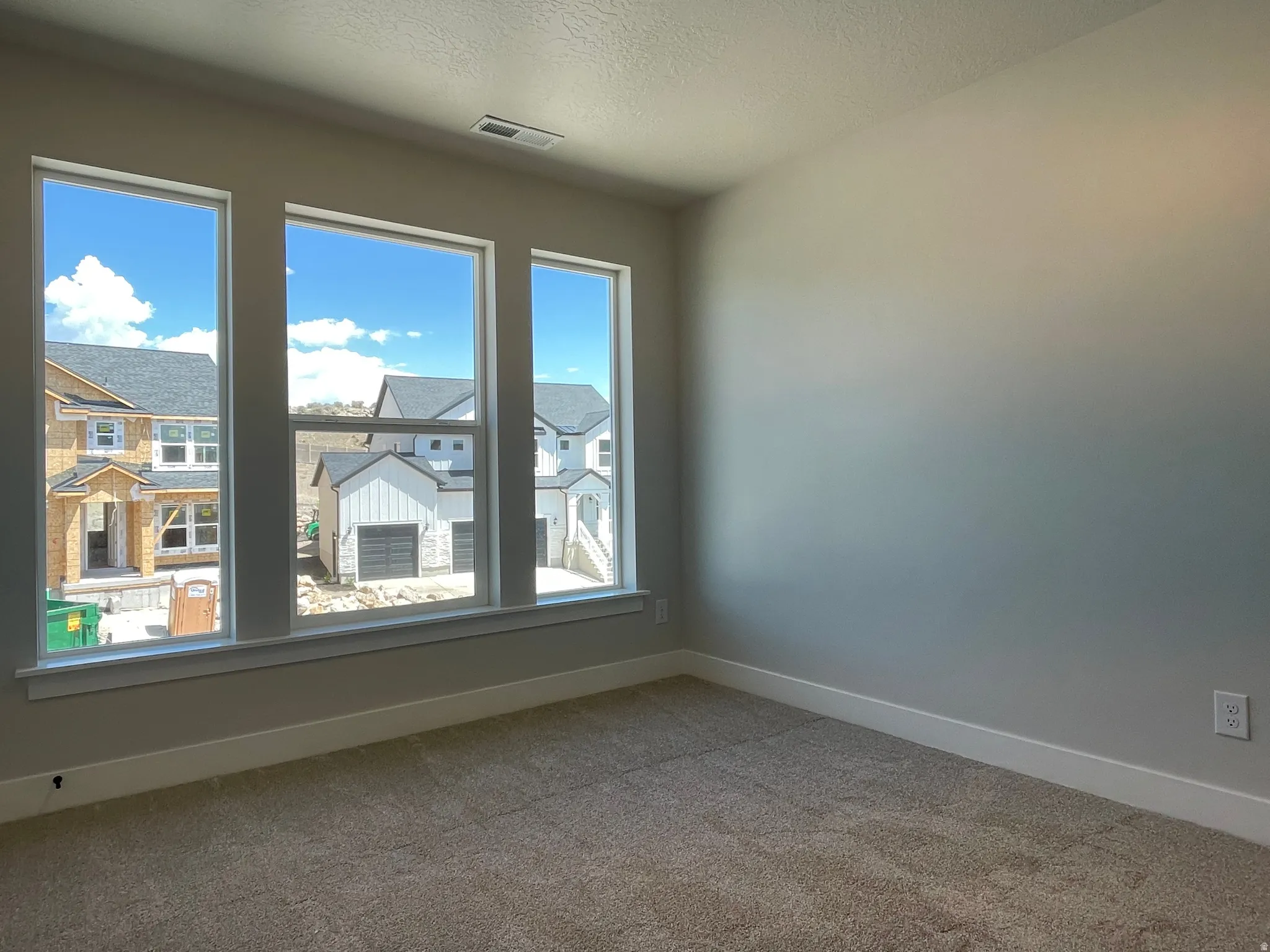 Interior room featuring a trio of vertical windows, neutral wall tones, white trim, and plush carpeting
