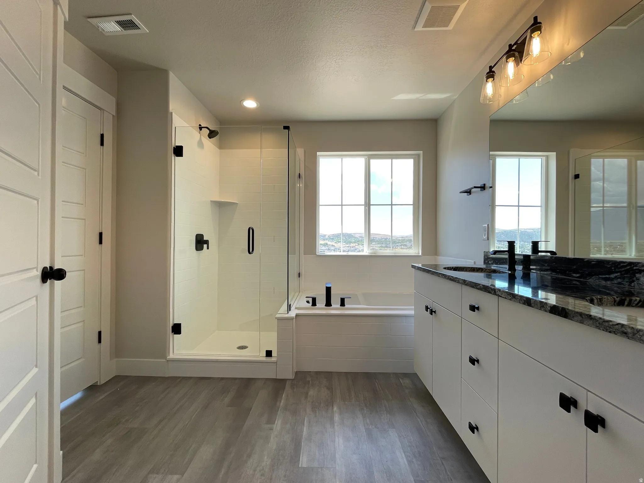 Contemporary bathroom featuring a spacious walk-in shower with clear glass enclosure, a built-in soaking tub, a double vanity with stone countertop, and wood-finish flooring