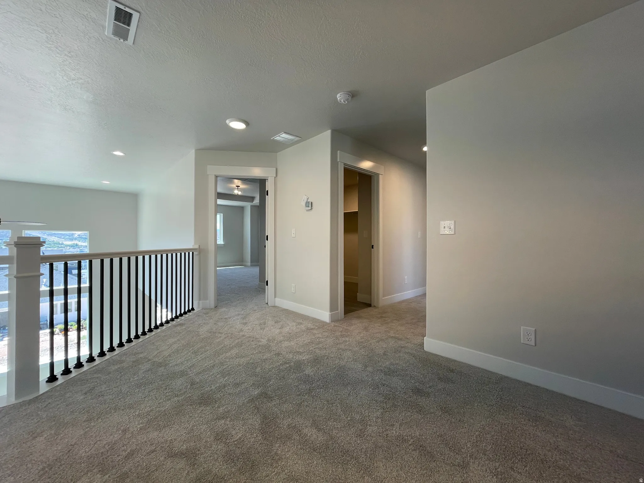 Carpeted upstairs landing featuring a modern black spindle railing, recessed lighting, and neutral wall tones