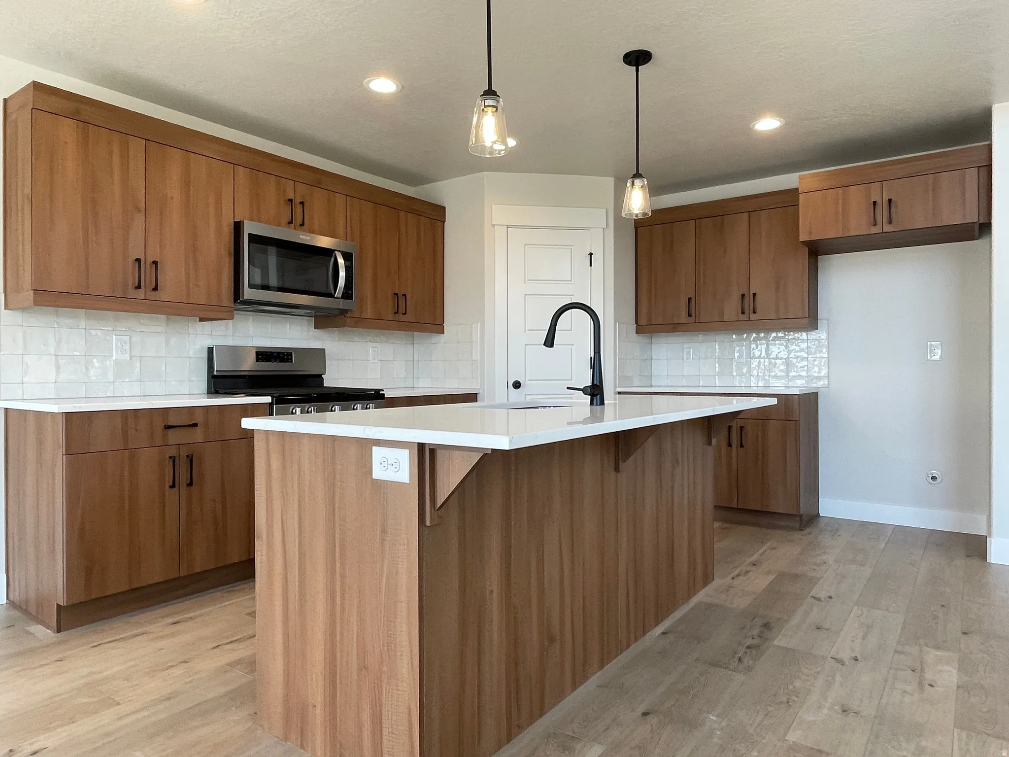 Kitchen featuring a central island, wood-finish cabinetry, stainless steel appliances, white subway tile backsplash, and light wood-finish flooring