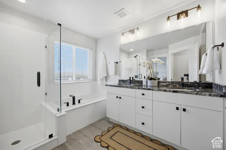 Spacious bathroom featuring a dual vanity with a dark stone countertop, a large frameless mirror, a built-in bathtub, and a glass-enclosed shower