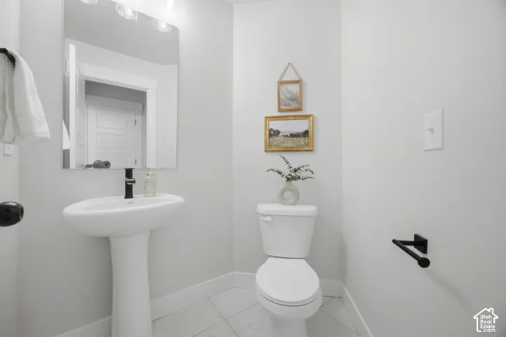 Pedestal sink with a black-finish faucet, rectangular wall-mounted mirror, and overhead vanity lighting