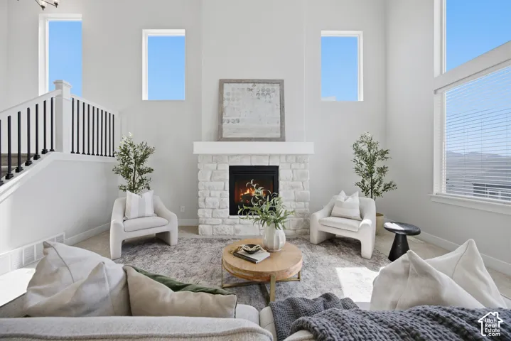 Two-story living area with a stone-clad fireplace and mantel, high ceilings, multiple windows, and a staircase featuring black metal balusters