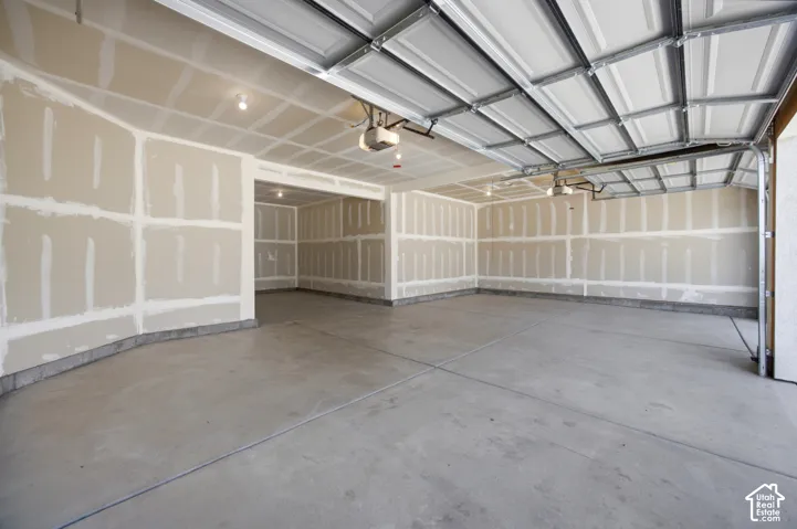 Spacious interior with concrete flooring, exposed drywall, overhead lighting, and an automated garage door