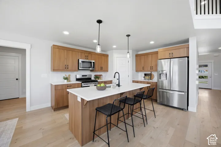Modern kitchen featuring wood-finish cabinetry, stainless steel appliances, a white subway tile backsplash, a center island with white countertops, and light wood-finish flooring