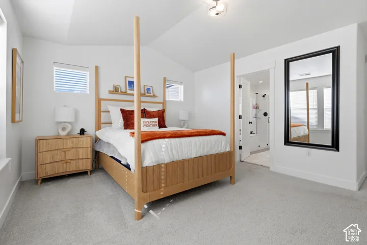 Vaulted ceiling, two windows with blinds, recessed wall shelf, wall-mounted mirror, and attached three-quarter bathroom with glass-enclosed shower