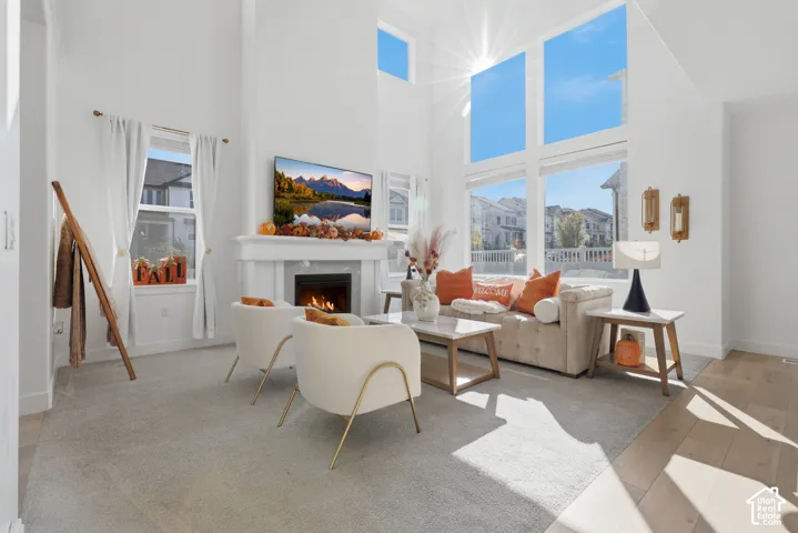 Bright, light-filled living room showcasing soaring ceilings with skylights, a gas fireplace with surround mantel, expansive windows framing natural scenery, wood-finish flooring, and modern architectural details throughout