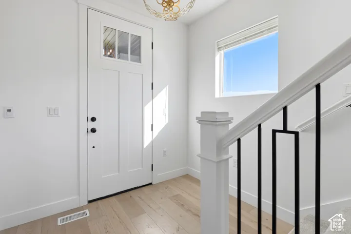 Bright entryway featuring a white six-panel entry door with glass panels, wide-plank wood-finish flooring, modern black metal stair railings, and abundant natural light from a substantial window