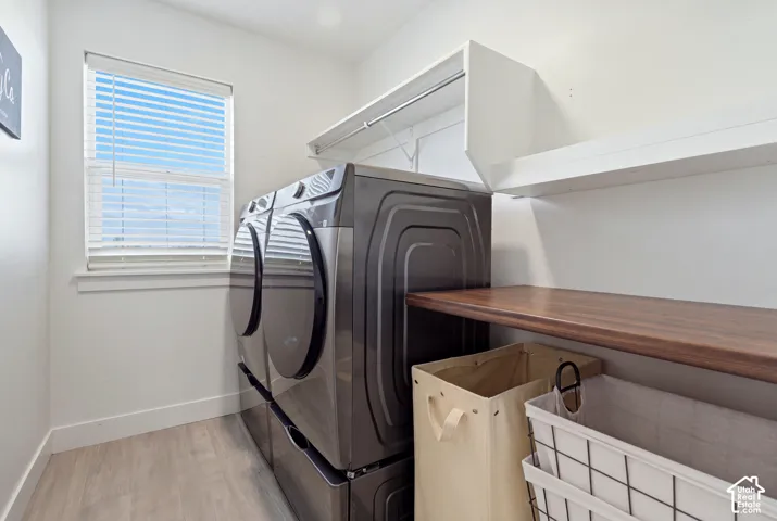 Dedicated laundry space featuring a white window, light wood-finish flooring, two white wall-mounted shelves, and a wood-finish countertop